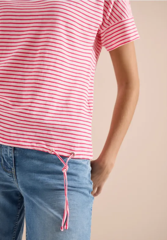 Eine Person trägt ein kurzärmeliges rot-weiß gestreiftes T-Shirt mit Tunnelzug am Saum und blaue Jeans.