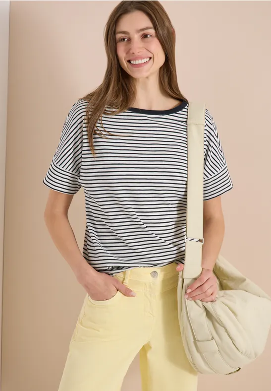 Frau trägt gestreiftes Shirt, breite gelbe Hose und großen gesteppten Beutel.