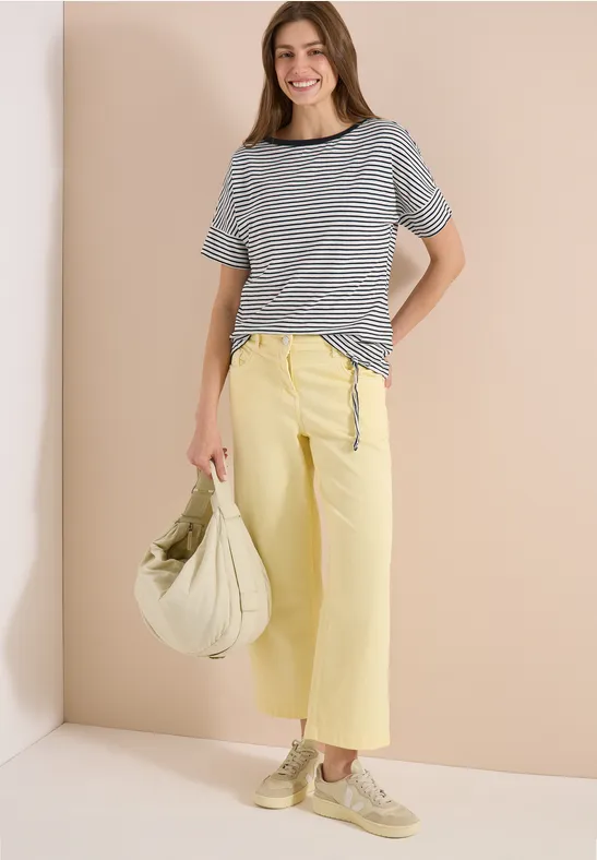 Frau trägt gestreiftes Kurzarmshirt und gelbe weite Culotte, dazu helle Tasche und Schuhe.