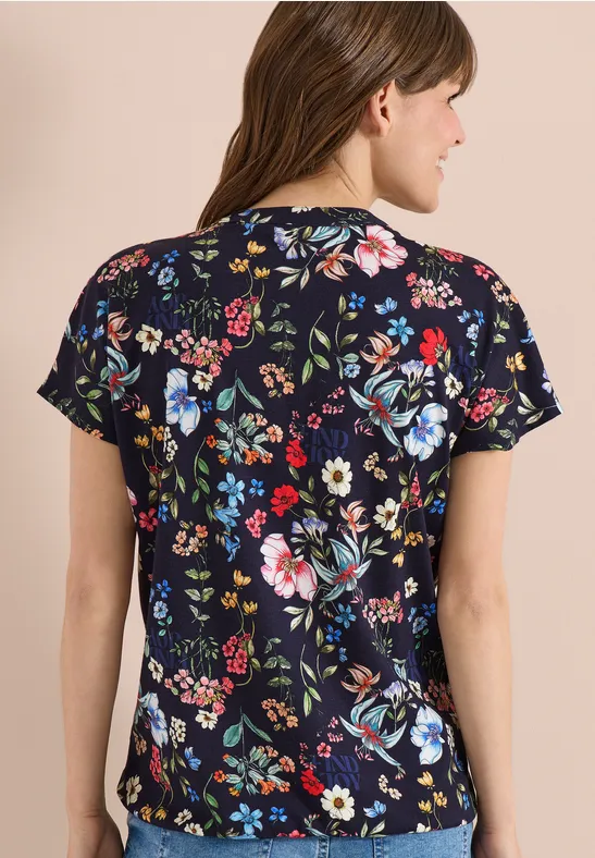 Een persoon van achteren in een donkerblauw T-shirt met gekleurde bloemenprint.