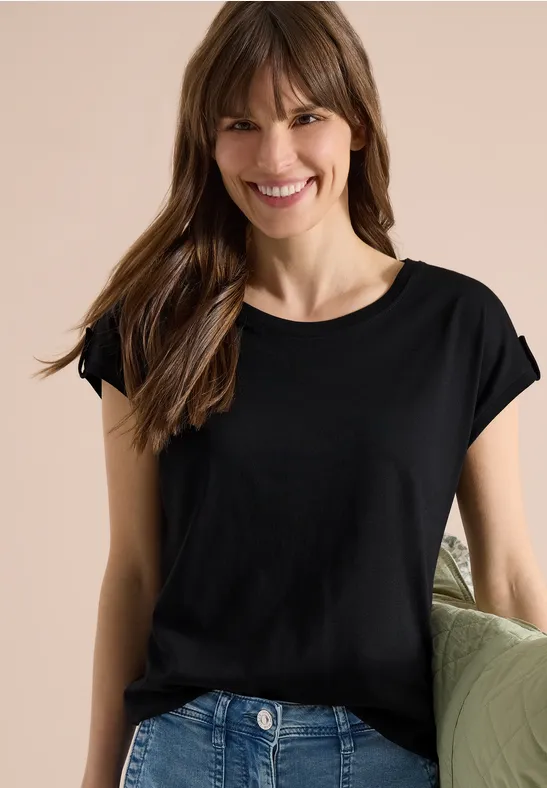 Eine Frau in einem schlichten schwarzen T-Shirt, hält ein hellgrünes Kissen in der Hand.