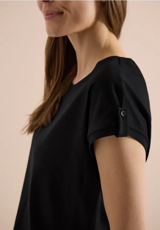 Eine Frau trägt ein schwarzes T-Shirt mit hochgekrempelten Ärmeln.