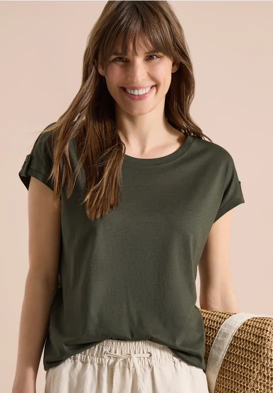Frau trägt schlichtes olivgrünes T-Shirt und helle Hose.
