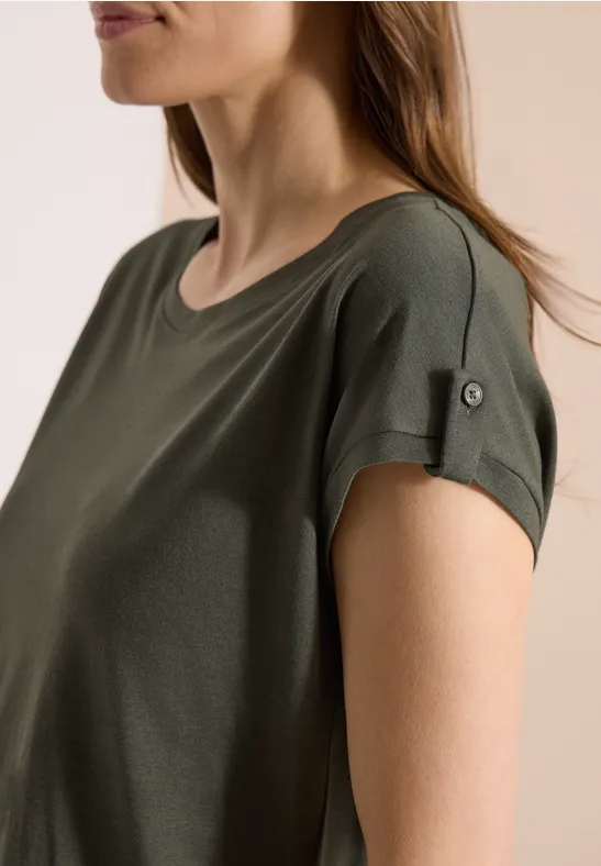 Frau im Profil trägt ein kurzärmeliges, olivgrünes T-Shirt mit aufgekrempelten Ärmeln.