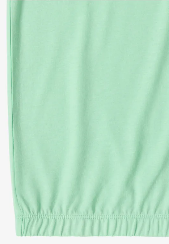 Onderkant van een muntgroen kledingstuk met elastische zoom tegen een witte achtergrond.