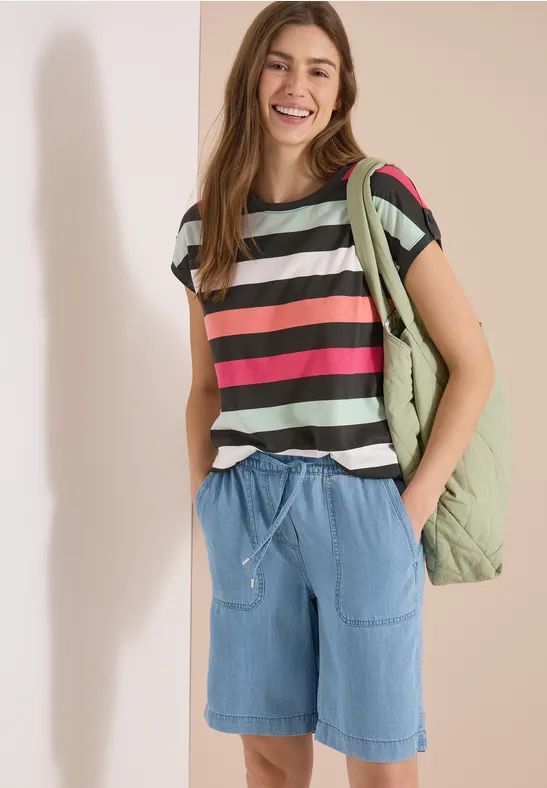 Personne portant un t-shirt rayé, un short en jean et un sac à dos, posant devant un fond neutre.