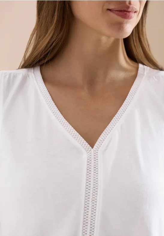 Close-up van een vrouw in een wit V-halsshirt met fijne kanten rand langs de hals.