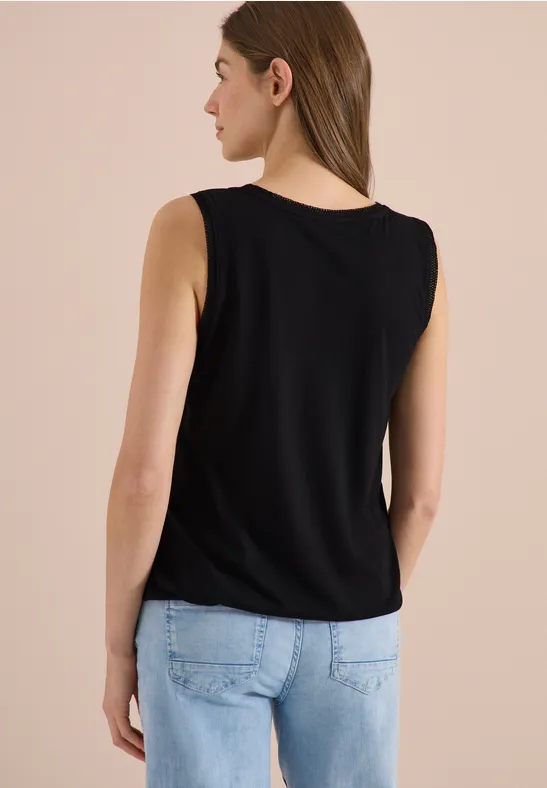 Vrouw van achteren in een zwart mouwloos shirt en lichtblauwe jeans voor een effen achtergrond.