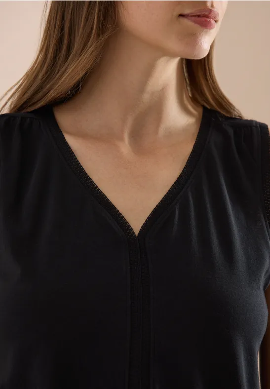 Close-up van een vrouw in een zwarte V-hals top, waarbij nek, schouders en een deel van het gezicht zichtbaar zijn.