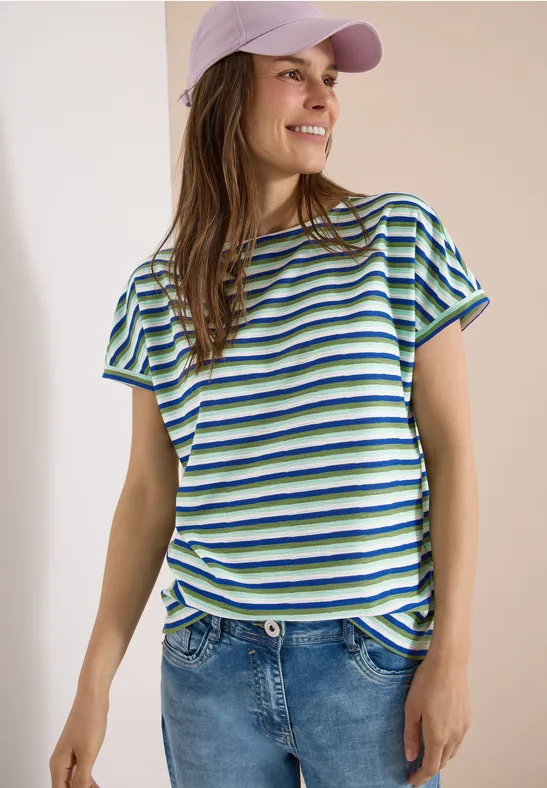 Vrouw draagt gestreept blauw-groen-wit T-shirt met jeans en pet.