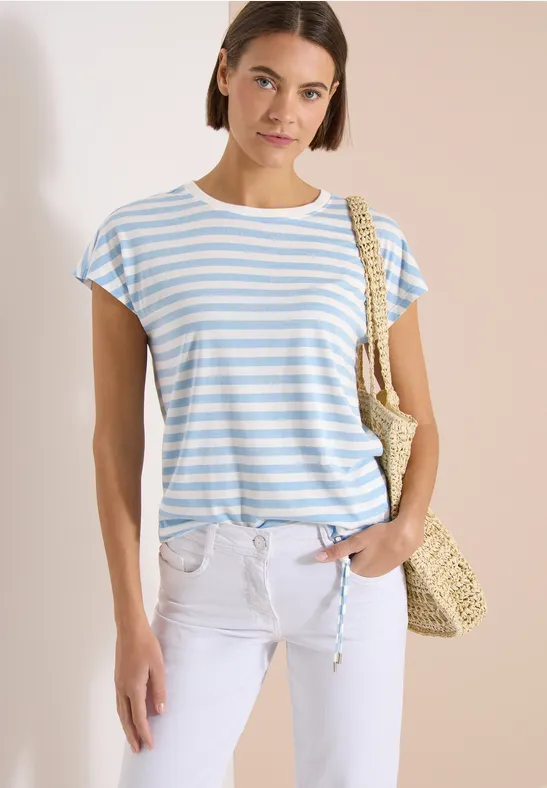 Frau in blau-weiß gestreiftem T-Shirt, weißer Hose und Strohtasche.