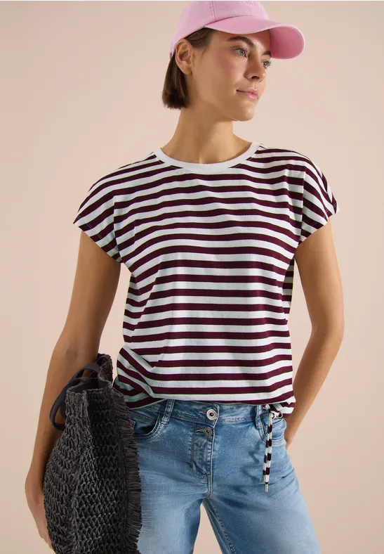 Femme en T-shirt rayé blanc et foncé à manches courtes, jean bleu clair, sac en maille et casquette.