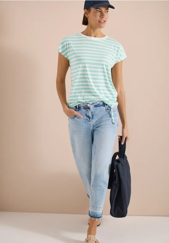 Femme en t-shirt rayé vert menthe et blanc, jean clair retroussé, tenant une veste foncée.