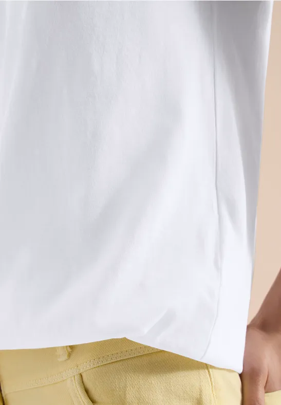 Person im weißen T-Shirt und senfgelben Hosen vor beigem Hintergrund