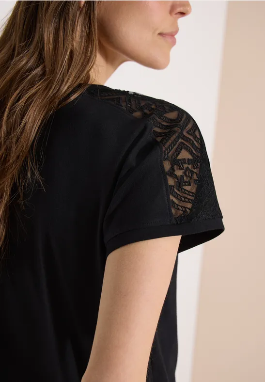 Schwarzes T-Shirt mit kurzen Ärmeln und transparenten Spitzen-Einsätzen auf den Schultern, Blick von hinten.