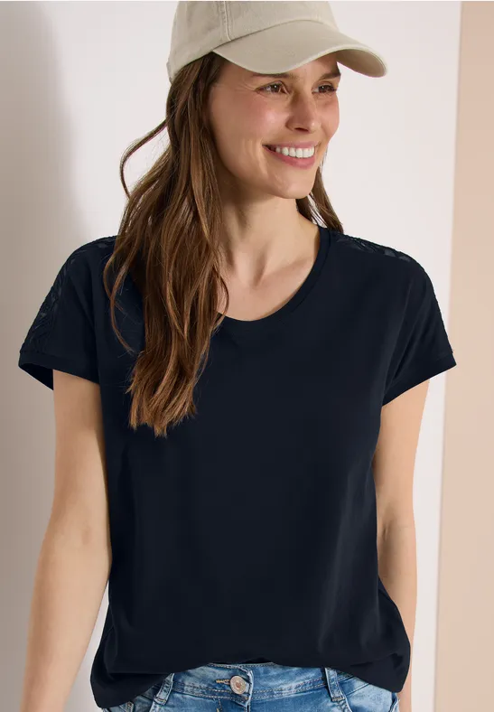 Vrouw met zwart T-shirt en pet, voor een neutrale achtergrond.