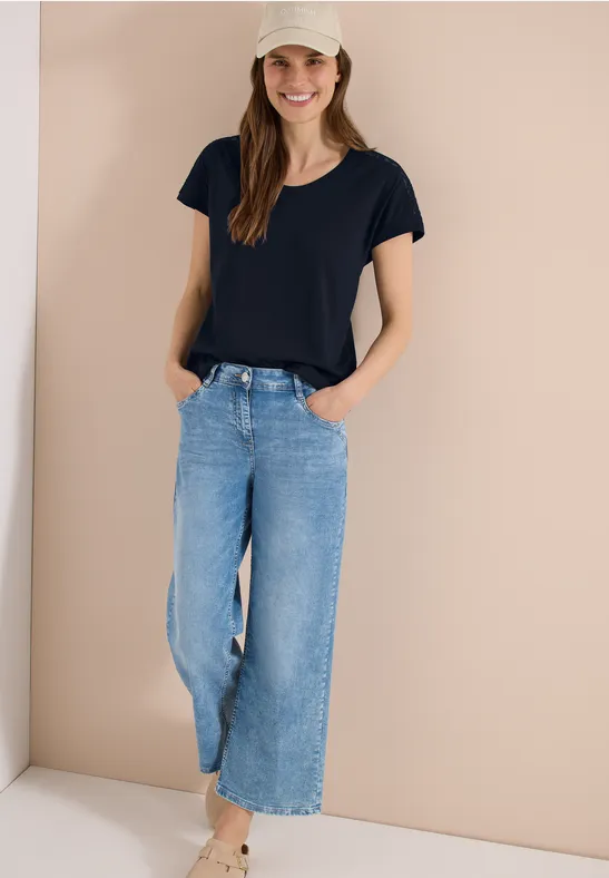 Vrouw met zwart t-shirt en ruime lichtblauwe jeans, ontspannen staand met handen in de zakken.