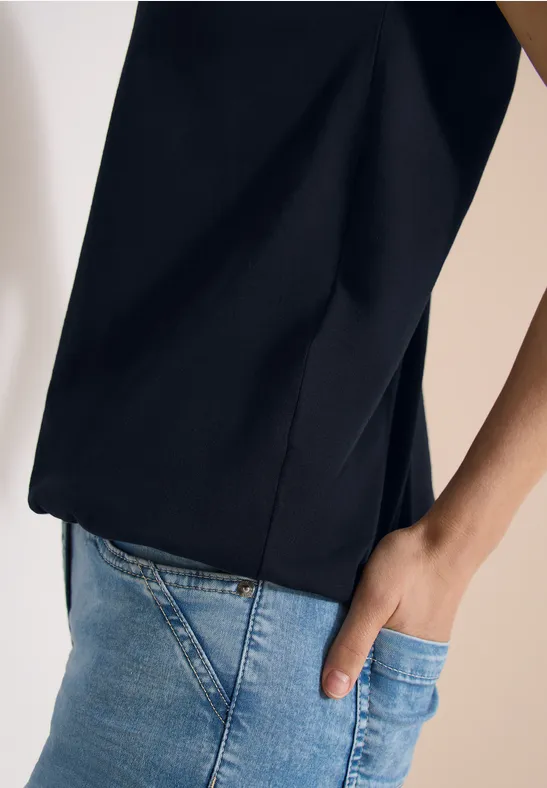 Persoon draagt zwarte top en lichte spijkerbroek, rechterhand in zak