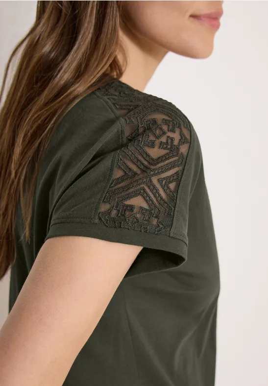 T-shirt olive à manches courtes avec empiècement en dentelle géométrique sur l'épaule.