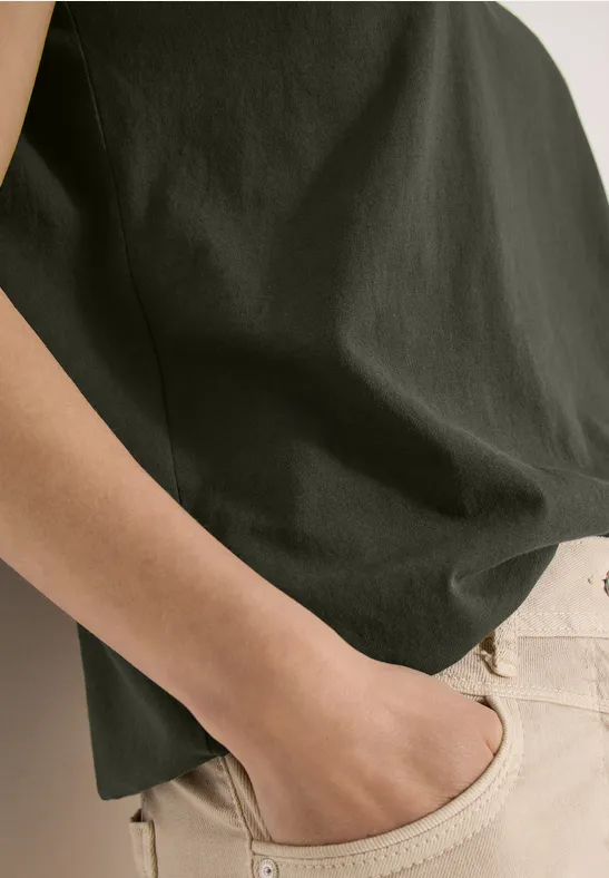 Une personne porte un t-shirt sombre et un pantalon clair, main détendue dans la poche.