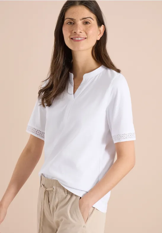 Frau in weißem Shirt mit Spitzenärmeln und beiger Hose.