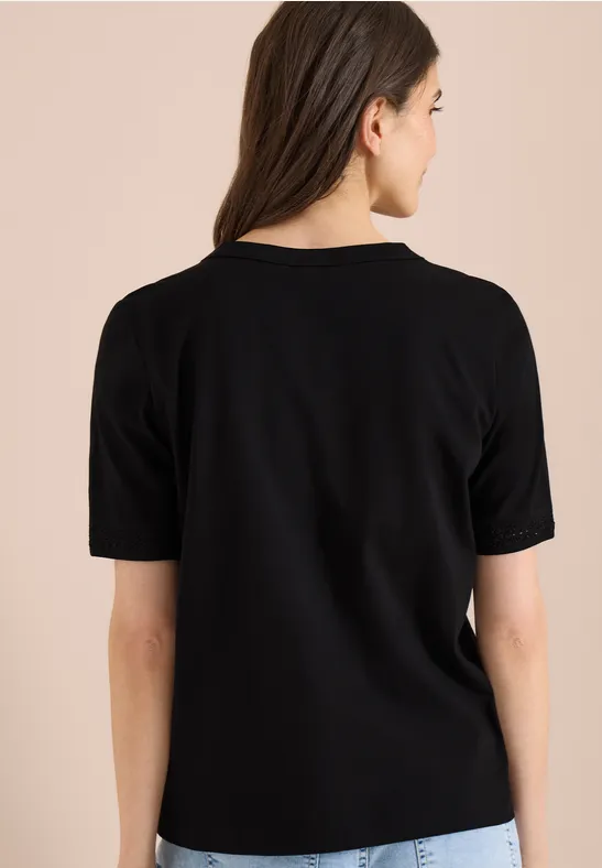 Vrouw van achteren in een effen zwart T-shirt met korte mouwen tegen een neutrale achtergrond.