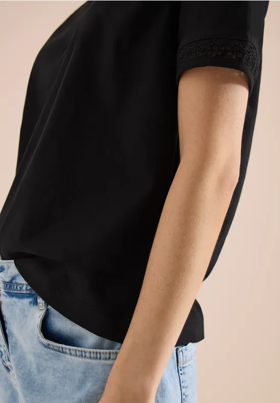 Vrouw in zwart T-shirt en spijkerbroek, hand nonchalant in de zak.