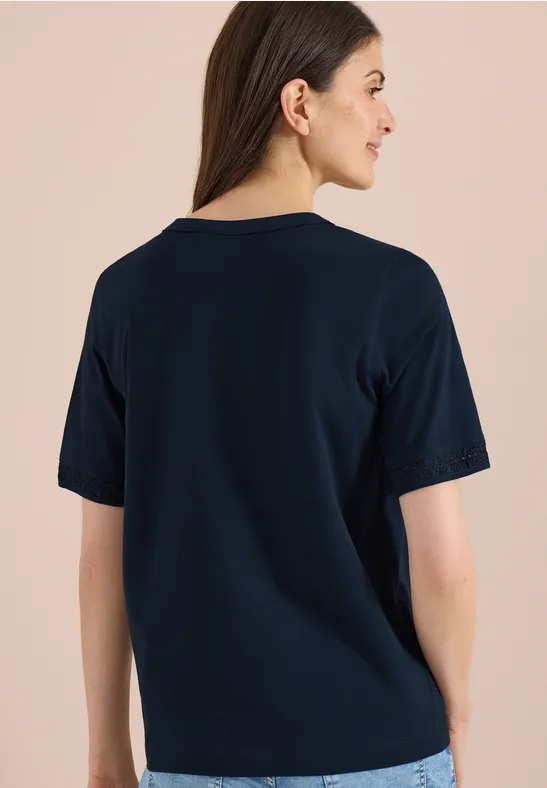 Vrouw van achteren in een donkerblauw T-shirt voor een beige achtergrond.