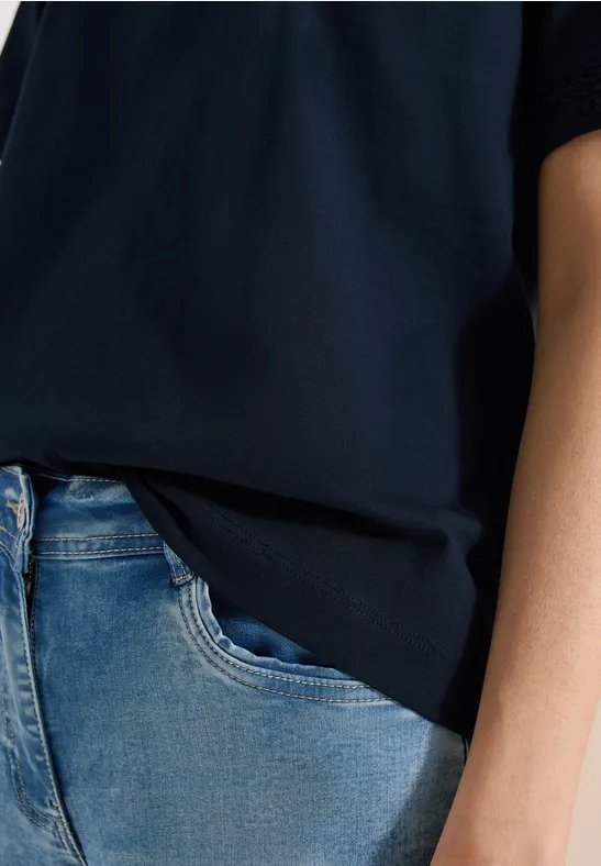 Een persoon draagt een donkerblauw T-shirt en een lichtblauwe spijkerbroek, alleen de torso is zichtbaar.