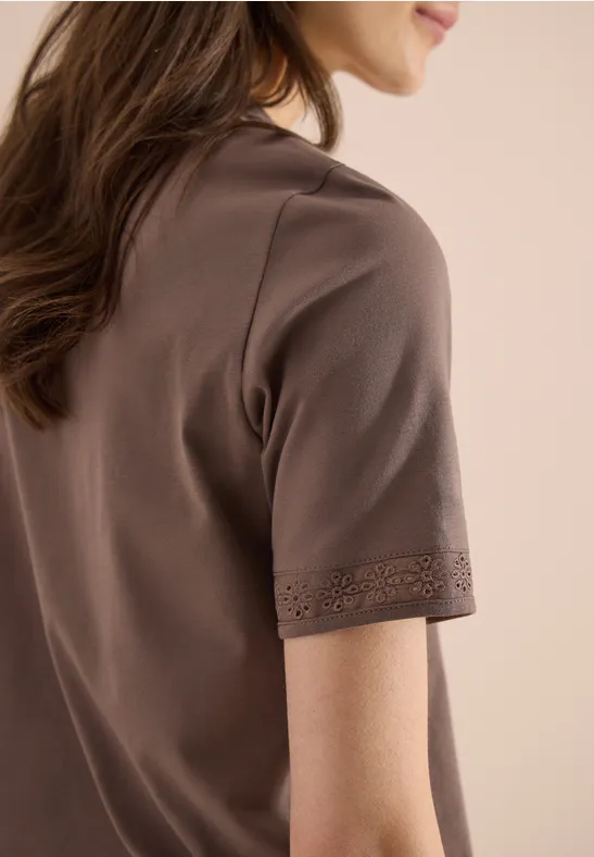 Zijaanzicht van een vrouw in een bruin T-shirt met korte mouwen en een sierlijke zoom.