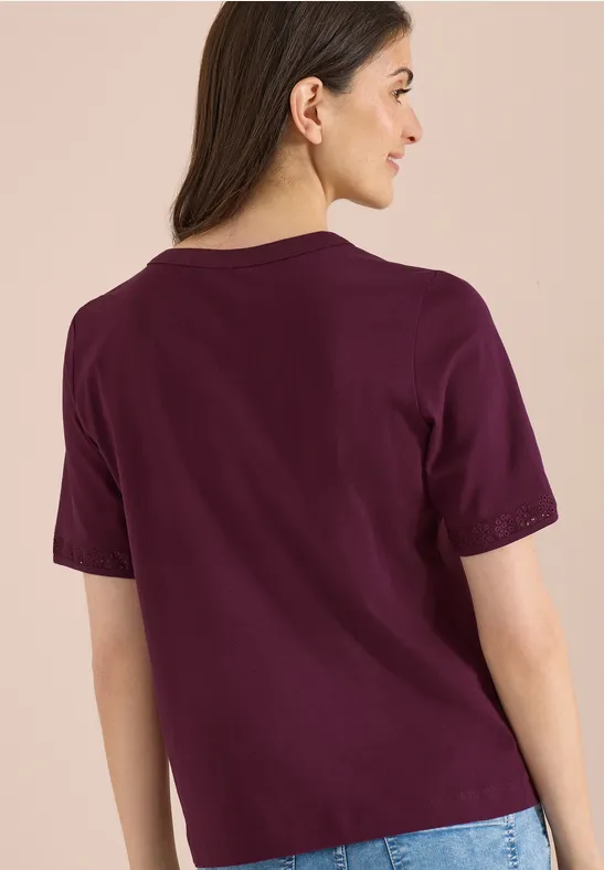 Vrouw van achteren in een losvallend paars T-shirt tegen een lichtbeige achtergrond.