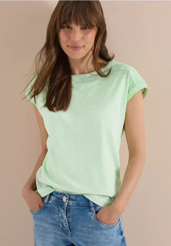 Femme en T-shirt vert clair et jean bleu, mains dans les poches.