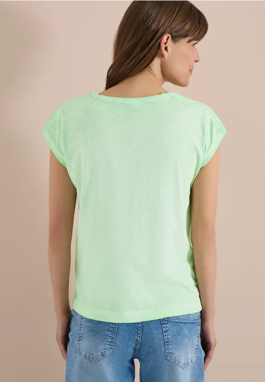 Femme vue de dos portant un t-shirt vert fluorescent devant un mur clair.