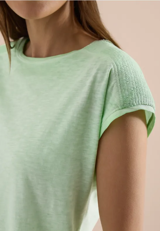 Femme portant un t-shirt vert clair avec tissu structuré aux épaules