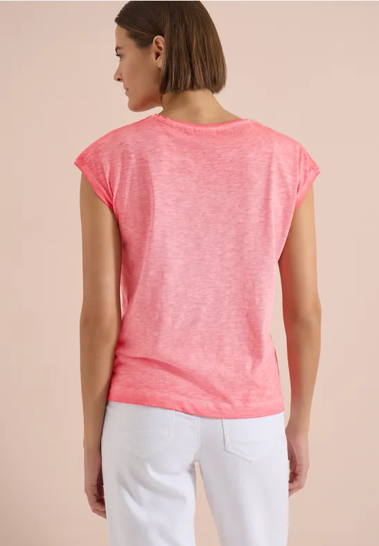 Eine Frau von hinten mit pinkem T-Shirt und weißen Jeans vor hellem Hintergrund.