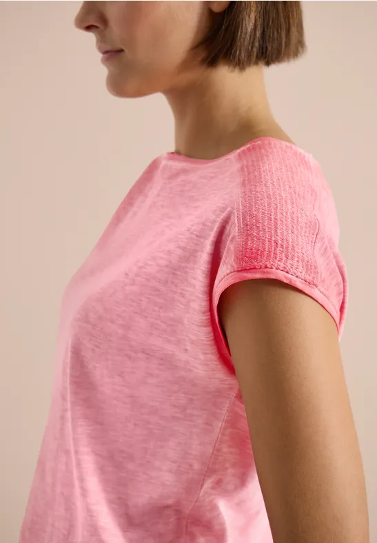 Seitliches Profil einer Person in einem pinkfarbenen kurzärmligen T-Shirt vor neutralem Hintergrund.