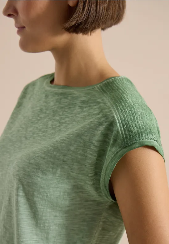 Frau mit kurzem Bob trägt ein hellgrünes, kurzärmeliges Shirt in nahem Porträt.