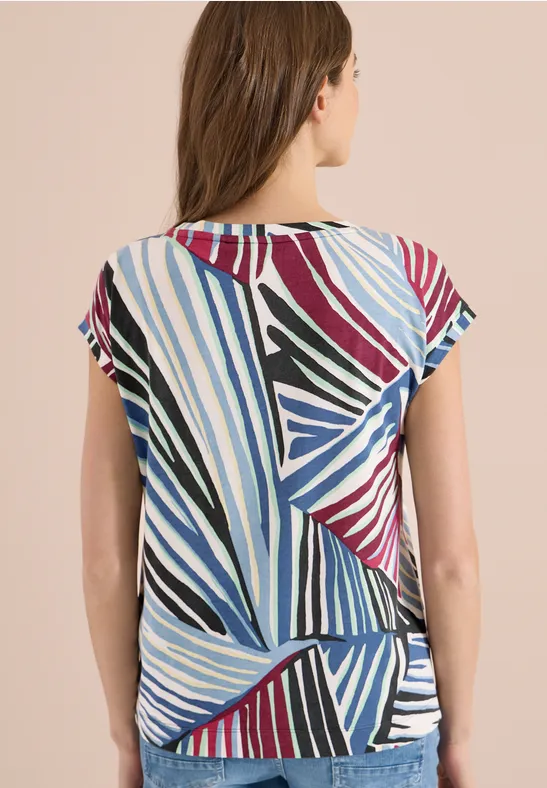 Frau von hinten in bunt gestreiftem, grafischem Kurzarmtop in Blau, Schwarz, Weiß, Rot und Grün.