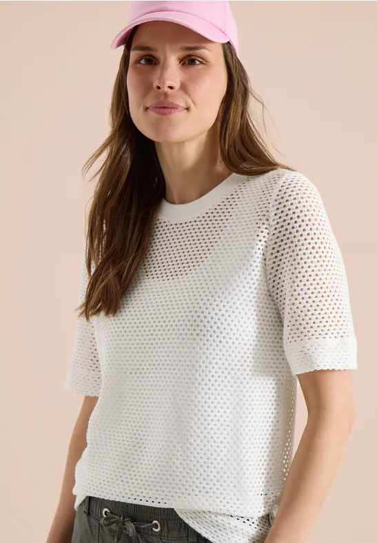 Model met lang bruin haar draagt een wit, halfdoorzichtig gaas-T-shirt met korte mouwen.