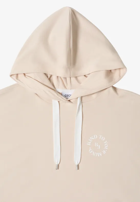 Hellbeiger Kapuzenpullover mit weißen Kordeln und kleinem weißen Schriftzug auf der Brust.