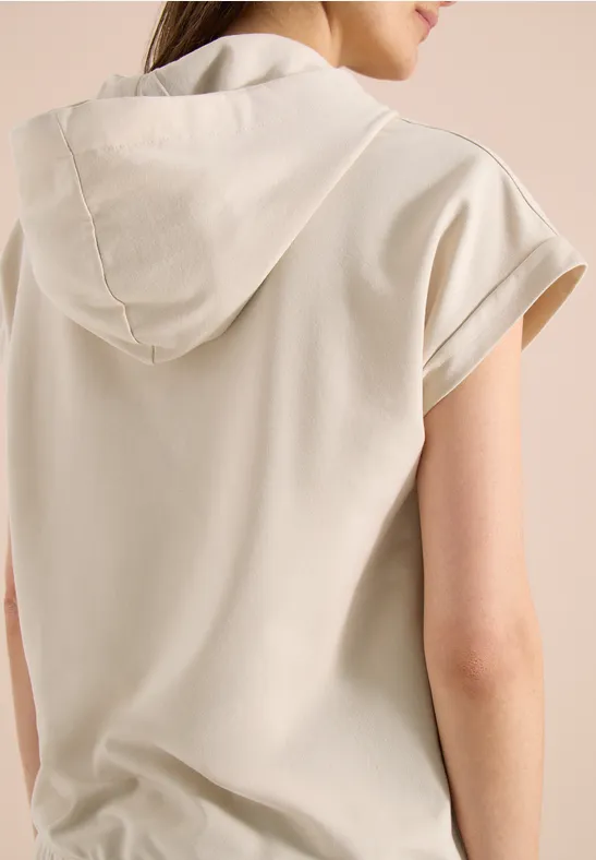 Frau in cremefarbenem Kapuzen-T-Shirt von hinten, kurze Ärmel, lässiger Look.