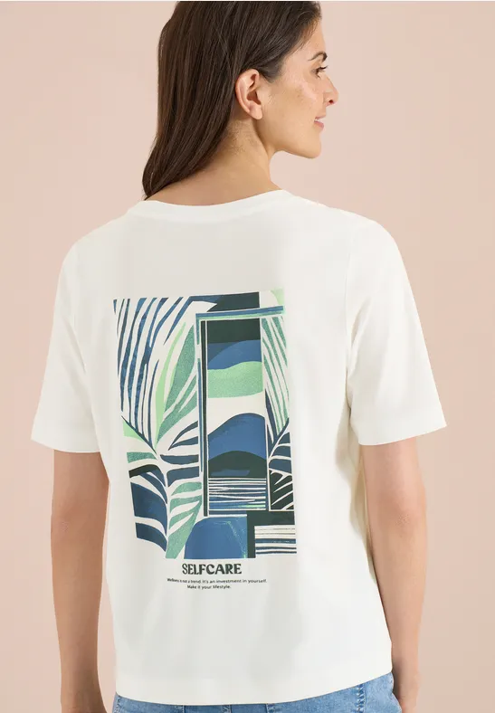 Frau von hinten in weißem T-Shirt mit grün-blauem, abstraktem Muster und „SELFCARE“-Schriftzug.