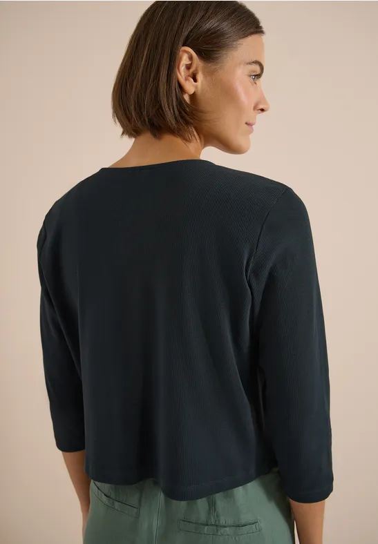 Achteraanzicht van persoon met kort bobkapsel en donkergroen kort vest met driekwartmouwen.