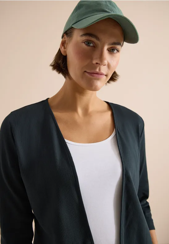 Bovenlichaam van persoon in zwart jasje, wit topje en groene pet, gezicht onscherp.