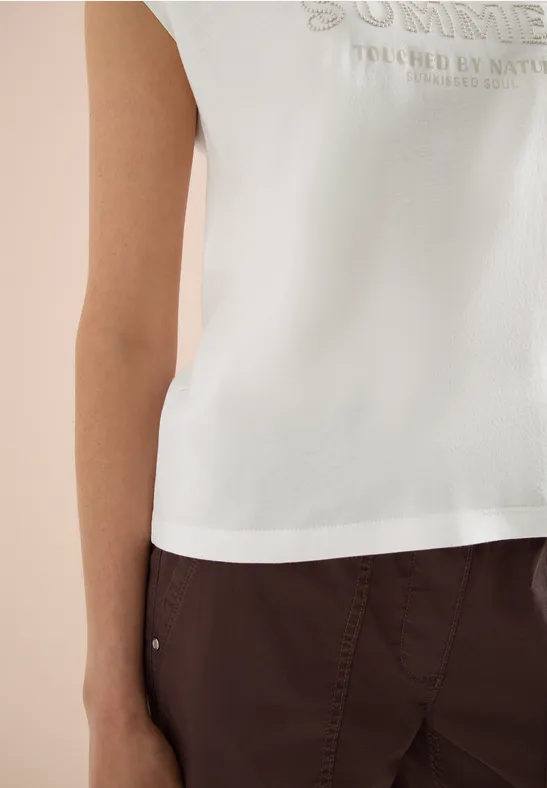 Persoon draagt een mouwloos wit topje met opdruk en een donkerbruine broek, torso zichtbaar