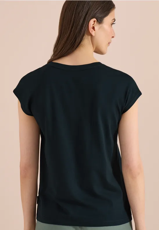 Jonge vrouw van achteren in zwart T-shirt met korte mouwen, bruin haar tegen een beige achtergrond.