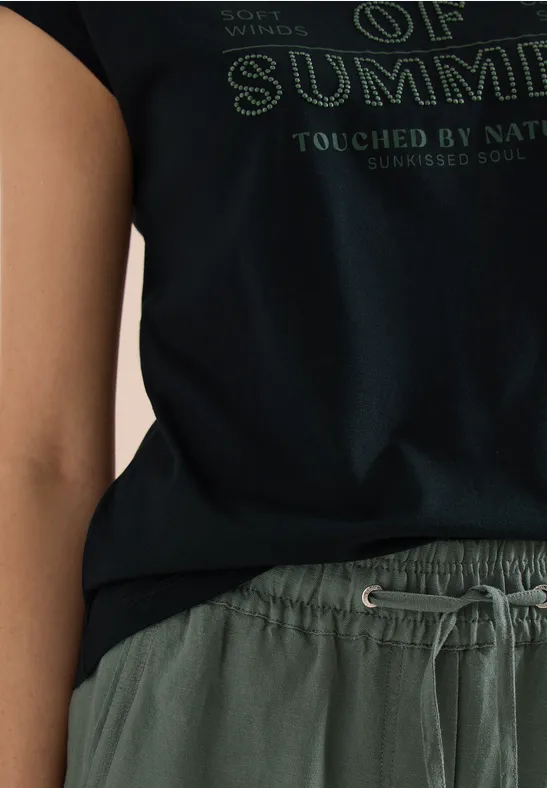 Close-up van persoon in zwart T-shirt met opdruk "OF SUMMER" en groene short met trekkoord.