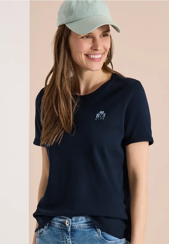 Frau in dunkelblauem Poloshirt, hellblauer Baseballkappe und Jeans, Gesicht unkenntlich.