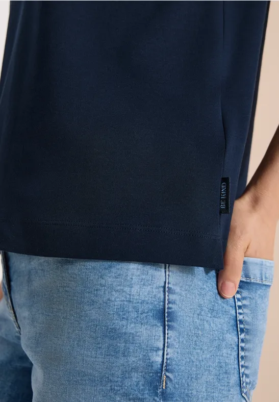 Nahaufnahme von dunkelblauem T-Shirt und hellblauer Jeanshose, Hand steckt in Tasche.