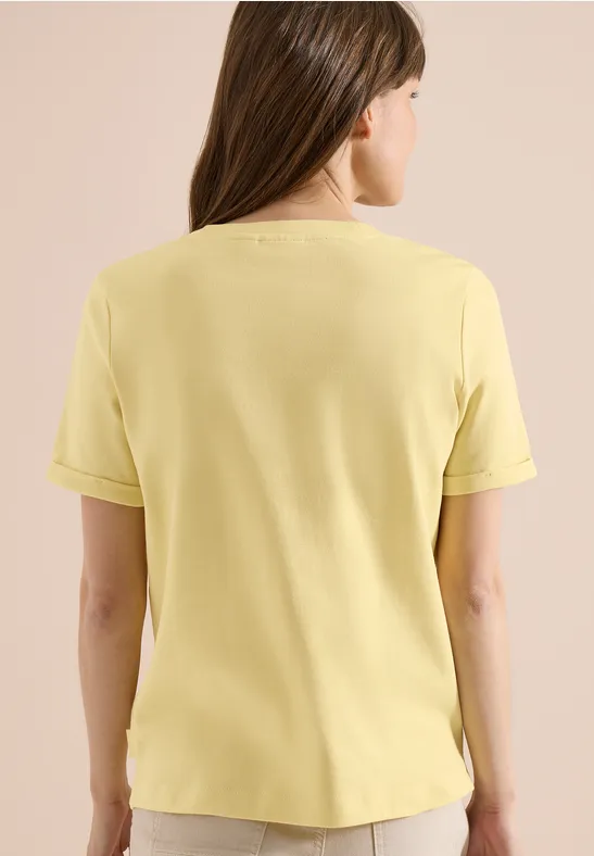 Eine Frau von hinten, die ein hellgelbes Kurzarmshirt trägt vor hellem Hintergrund.